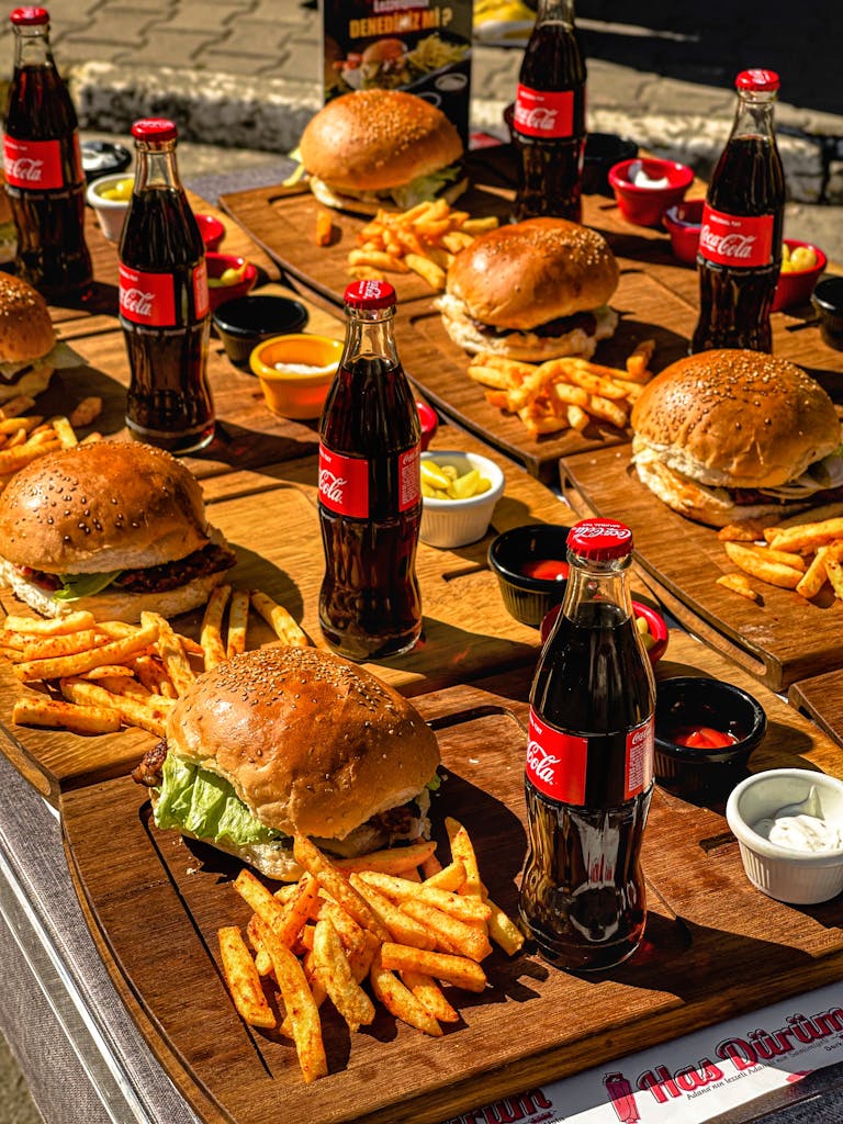 Appetizing burgers with fries and Coca-Cola bottles served outdoors on wooden trays under sunny skies.